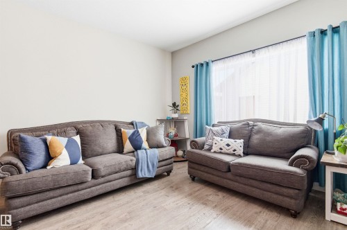Living area featuring light colored walls, wood-style flooring, and a window with light blue curtains - 678 Secord Boulevard, Edmonton, AB - Indoor Photo Showing Living Room