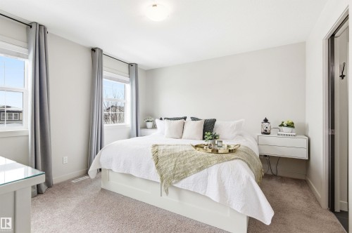 This room features neutral-toned carpet, two windows with blinds and curtains, and a light-colored accent wall - 678 Secord Boulevard, Edmonton, AB - Indoor Photo Showing Bedroom
