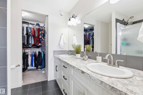 Bathroom featuring a dual vanity with white cabinets, a light-colored countertop, and two undermount sinks with brushed nickel faucets - 678 Secord Boulevard, Edmonton, AB - Indoor Photo Showing Bathroom