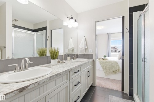 This bathroom features a dual vanity with a light-colored countertop and white cabinetry - 678 Secord Boulevard, Edmonton, AB - Indoor Photo Showing Bathroom
