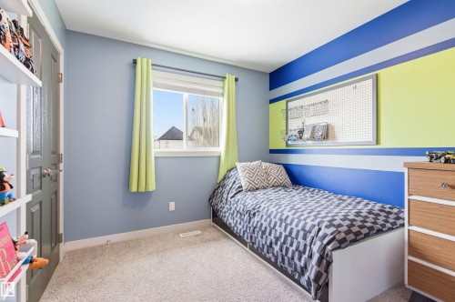 This room features a window with light green curtains, carpeted flooring, and a door with a frosted glass panel - 678 Secord Boulevard, Edmonton, AB - Indoor Photo Showing Bedroom