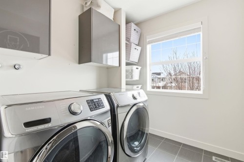 This functional laundry area features gray tile flooring, white walls, and a window providing natural light - 678 Secord Boulevard, Edmonton, AB - Indoor Photo Showing Laundry Room
