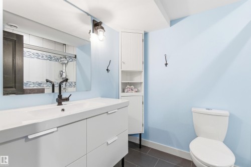 The bathroom features a modern vanity with an integrated sink and a sleek black faucet, a large mirror, and tiled floors - 678 Secord Boulevard, Edmonton, AB - Indoor Photo Showing Bathroom
