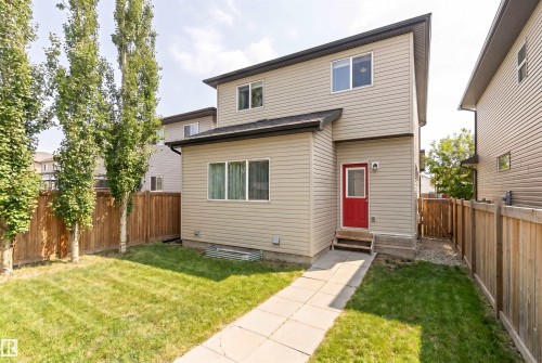 The property features a two-story exterior with light-colored siding, a red entrance door, and a well-maintained lawn - 678 Secord Boulevard, Edmonton, AB - Outdoor With Exterior