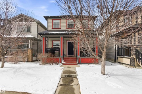 The property features a two-story exterior with light-colored siding, red trim around the windows, and a covered porch with red support columns and steps - 678 Secord Boulevard, Edmonton, AB - Outdoor