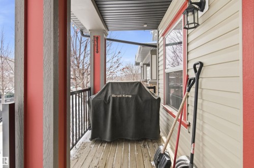 This property features a covered balcony with wood-planked flooring, a black metal railing, and an outdoor wall lantern - 678 Secord Boulevard, Edmonton, AB -  With Exterior