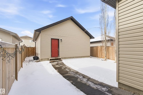 Detached garage with beige siding, a dark roof, and a red door - 678 Secord Boulevard, Edmonton, AB - Outdoor With Exterior