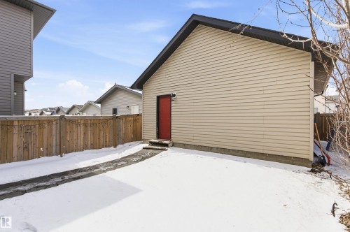 Detached garage with beige siding and a red side door, featuring a paved path and a wooden fence - 678 Secord Boulevard, Edmonton, AB - Outdoor With Exterior