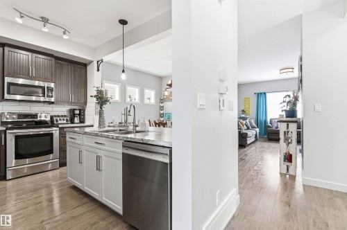 The property features a kitchen with dark wood upper cabinetry, white lower cabinetry, and stainless steel appliances - 678 Secord Boulevard, Edmonton, AB - Indoor Photo Showing Kitchen With Double Sink With Upgraded Kitchen
