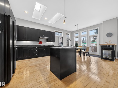 Open concept kitchen featuring light wood flooring, dark cabinetry, and two skylights - 569 Butterworth Way, Edmonton, AB - Indoor Photo Showing Kitchen With Upgraded Kitchen