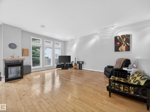 This living area features hardwood floors, a modern fireplace with a light wood mantel, and large windows that provide abundant natural light - 569 Butterworth Way, Edmonton, AB - Indoor Photo Showing Living Room With Fireplace