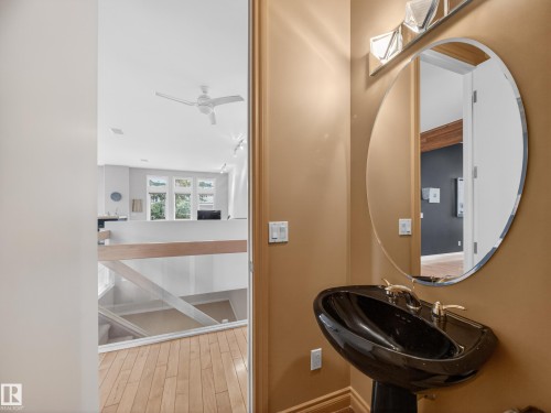 This property features a black pedestal sink with a gold faucet, a large oval mirror with a beveled edge, and light wood flooring - 569 Butterworth Way, Edmonton, AB - Indoor