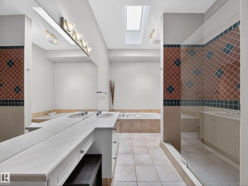 Bathroom featuring a spacious vanity with two integrated sinks and an expansive mirror, a tiled shower with a glass enclosure, and a separate bathtub - 569 Butterworth Way, Edmonton, AB - Indoor