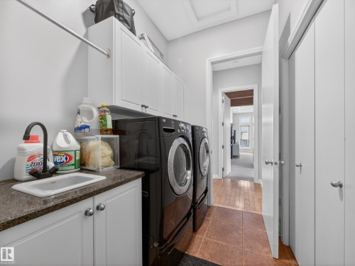 Laundry room featuring white cabinetry, a sink with a dark faucet, and a granite-style countertop - 569 Butterworth Way, Edmonton, AB - Indoor Photo Showing Laundry Room
