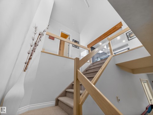 The property features a staircase with light wood banisters and glass panels, complemented by carpeted stairs - 569 Butterworth Way, Edmonton, AB - Indoor Photo Showing Other Room