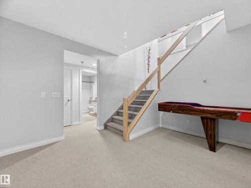 The property features a staircase with light wood banister and glass panels, light-colored carpeting, and a doorway leading to a room with a visible toilet and vanity - 569 Butterworth Way, Edmonton, AB - Indoor Photo Showing Other Room