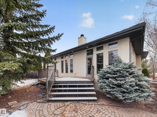The property features an exterior with light-colored stucco and a dark-colored roof, complemented by a wooden deck with stairs leading to a paved patio - 569 Butterworth Way, Edmonton, AB - Outdoor