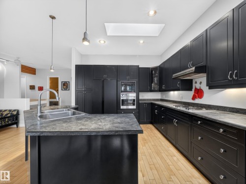 Contemporary kitchen featuring dark cabinetry, stone countertops, a stainless steel sink with a gooseneck faucet, and light wood flooring - 569 Butterworth Way, Edmonton, AB - Indoor Photo Showing Kitchen With Double Sink With Upgraded Kitchen
