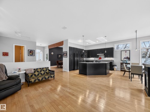 Open concept living area featuring light hardwood floors, a kitchen with dark cabinetry and a central island, and a dining area with views of the outdoors - 569 Butterworth Way, Edmonton, AB - Indoor