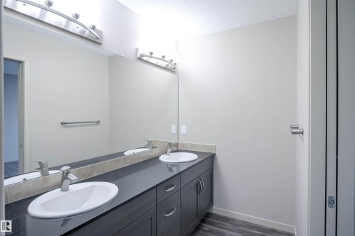 Hallway with wood-style flooring and white closet doors, leading to a bathroom featuring a dark vanity with an integrated sink and a wall-mounted mirror - 1426 25 Avenue, Edmonton, AB - Indoor