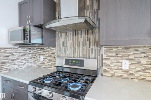 The kitchen features grey cabinetry, stainless steel appliances, and a tiled backsplash - 1426 25 Avenue, Edmonton, AB - Indoor Photo Showing Kitchen With Upgraded Kitchen