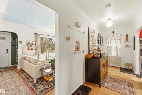 Bright interior hallway with light wood-finish flooring, featuring a decorative wall niche and a window with natural light - 6036 106 Street, Edmonton, AB - Indoor