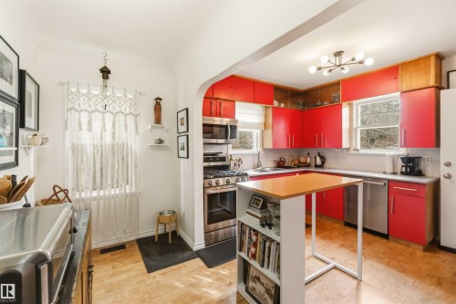 Contemporary kitchen featuring red cabinetry, stainless steel appliances, a white tile backsplash, a built-in island with shelving, and light wood-finish flooring - 6036 106 Street, Edmonton, AB - Indoor Photo Showing Kitchen