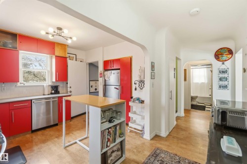 Kitchen featuring vibrant red cabinetry, stainless steel appliances, a white subway tile backsplash, and wood-finish flooring - 6036 106 Street, Edmonton, AB - Indoor Photo Showing Kitchen