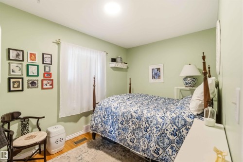 Bedroom featuring light green walls, hardwood flooring, and a window with white curtains - 6036 106 Street, Edmonton, AB - Indoor Photo Showing Bedroom