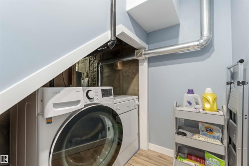 Dedicated laundry area featuring modern white appliances, light blue walls, and wood-finish flooring - 6036 106 Street, Edmonton, AB - Indoor Photo Showing Laundry Room