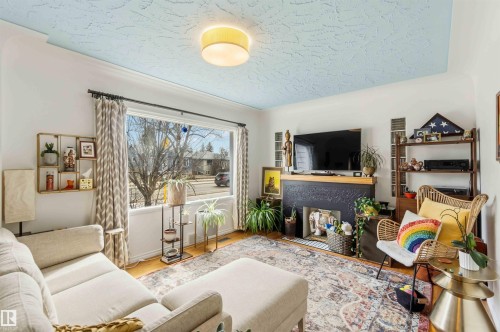 Living area featuring hardwood-finish flooring, crown molding, and a decorative fireplace with a black painted mantel - 6036 106 Street, Edmonton, AB - Indoor Photo Showing Living Room With Fireplace