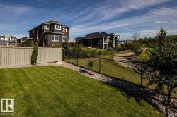 Expansive backyard featuring a manicured lawn, full-height privacy fencing, and a black chain-link fence bordering a paved pathway - 