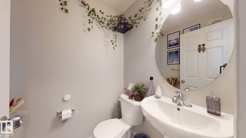 The bathroom features a pedestal sink, a toilet, and a circular mirror - 1275 Chappelle Boulevard, Edmonton, AB 
