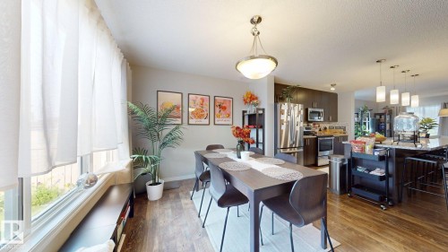 This inviting dining area features wood-style flooring, a modern chandelier, and a large window with sheer white curtains - 1275 Chappelle Boulevard, Edmonton, AB 