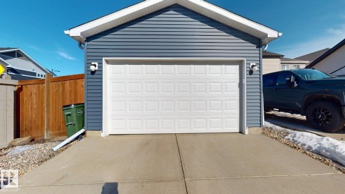 The property features a garage with blue siding and a white panel garage door, complete with outdoor sconce lighting - 1275 Chappelle Boulevard, Edmonton, AB 
