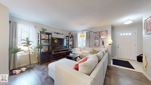 The living area features hardwood floors, light-colored walls, and a window with sheer and opaque curtains - 1275 Chappelle Boulevard, Edmonton, AB 