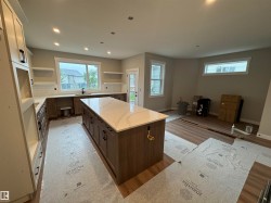 Spacious kitchen featuring a large central island with a light-toned countertop, recessed lighting, wood-finish flooring, and white subway tile backsplash - 