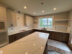 Spacious kitchen featuring an oversized island with a vein-patterned countertop, extensive perimeter countertops, two-tone cabinetry, white subway tile backsplash, and recessed lighting - 