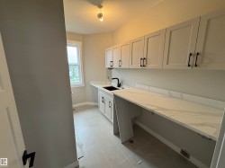 Laundry room featuring light gray cabinetry, white countertops with veining, an undermount black sink with a black gooseneck faucet, and light-toned tile flooring - 