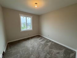 Well-lit interior space featuring neutral wall paint, a window with white trim, a semi-flush mount ceiling light, and patterned carpet flooring with white baseboards - 