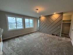 Spacious room featuring a decorative accent wall with geometric paneling, recessed lighting, and soft grey carpeting - 