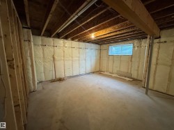 Unfinished basement featuring exposed wood joists and subflooring, framed interior walls, concrete slab flooring, and a single window - 