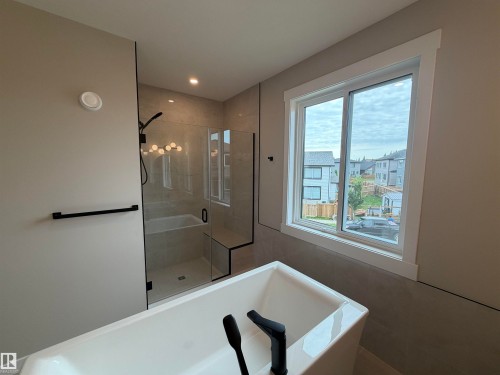 Freestanding soaking tub with a matte black faucet, walk-in shower with glass enclosure and bench seating, and tile surround - 33 Harley Way, Spruce Grove, AB - Indoor Photo Showing Bathroom