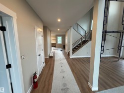 Open-concept interior featuring wood-finish flooring, a modern staircase with horizontal metal railings, and recessed ceiling lighting - 
