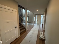Spacious entryway featuring wood-finish flooring, recessed lighting, a modern three-panel interior door with matte black hardware, and a staircase with metal railings - 