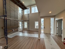 Two-story living area featuring wood-finish flooring, a contemporary fireplace with a wooden mantel, and a paneled accent wall - 