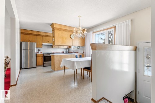 The kitchen features light wood cabinetry, stainless steel appliances, and an overhead chandelier light fixture - 10716 52 Avenue, Edmonton, AB - Indoor Photo Showing Kitchen