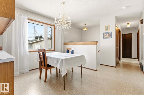 Dining area featuring a clear crystal chandelier, a window with white curtains, and light-colored flooring - 10716 52 Avenue, Edmonton, AB - Indoor Photo Showing Dining Room