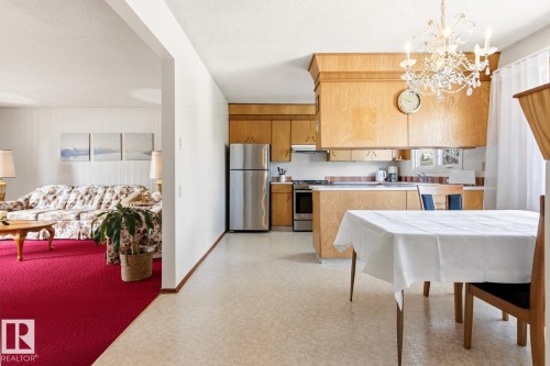 The property features a kitchen with wood cabinetry, stainless steel appliances, and a dining area with a chandelier - 10716 52 Avenue, Edmonton, AB - Indoor