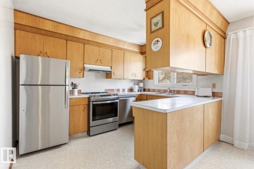 The kitchen features light wood cabinetry, stainless steel appliances, and white countertops - 10716 52 Avenue, Edmonton, AB - Indoor Photo Showing Kitchen